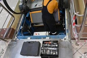 Man repairs escalator, steps inside, standing with her back near the step photo