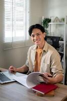 Smiling, satisfied Asian businessman is sitting at his desk in his office and smiling at the camera. photo