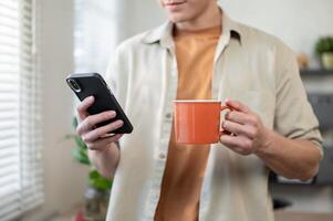 A man standing in his office, enjoying a coffee while reading messages on his smartphone. photo