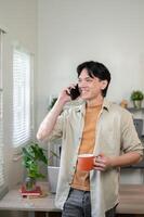 A smiling Asian businessman stands in his office, gazing out the window while talking on the phone. photo