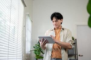 A happy Asian man stands in a room, using a digital tablet, drawing and designing his project. photo
