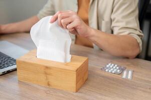 A close-up of a man reaching for a tissue from a tissue box while working at his desk in the office. photo