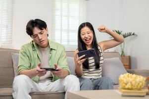 A joyful Asian couple enjoys racing a game on their smartphone, spending fun time at home together. photo