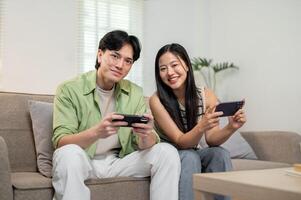 A lovely Asian couple sit on a sofa in the living room together, enjoying playing a mobile game. photo