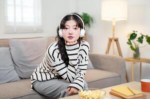 A pretty Asian woman wearing headphones, sitting on a sofa and looking directly at the camera. photo