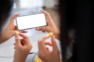 Two female friends chatting and snacking while watching a movie on a phone together on a sofa. photo