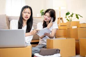 Women are busy at work. One is checking orders on a laptop, while the other is talking on the phone photo