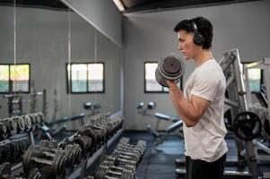 Focused Asian man is working out with a dumbbell in front of the dumbbell rack and mirror in the gym photo