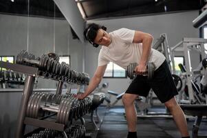 A muscular and handsome Asian man is working out with a dumbbell in front of the rack in the gym. photo
