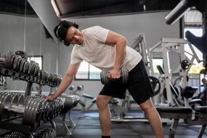 A handsome Asian man is working out with a dumbbell in front of the rack in the gym. photo