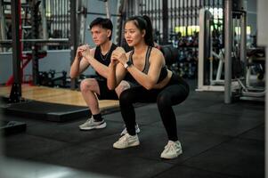 A side view of a determined Asian couple is training together in the gym, performing squats. photo