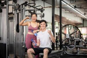 A cheerful and fit Asian people are smiling and showing a fist to the camera while standing in a gym photo