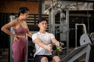 A supportive female fitness trainer is instructing a client in the gym on using the cable machine. photo