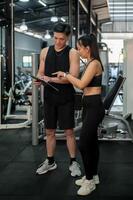 Athletic Asian male fitness instructor is discussing and adjusting a workout program with a client photo