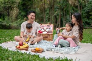 A lovely Asian family enjoys a picnic in a green park, sitting on a blanket and having fun together. photo