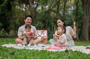 A happy Asian family enjoy picnic, mom and dad playfully blowing bubbles while their little kids. photo