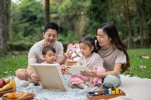 Lovely Asian parents take their little kids on a picnic in a park, enjoying painting on a canvas. photo
