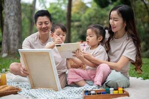 Lovely Asian parents take their little kids on a picnic, enjoying painting on a canvas together. photo