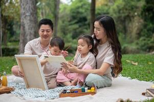 A happy and lovely Asian family enjoys painting on a canvas during a picnic in a public park. photo
