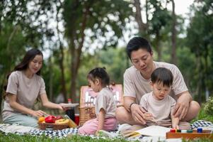 A caring Asian dad teaches his little son to draw and paint on a canvas while enjoying a picnic. photo