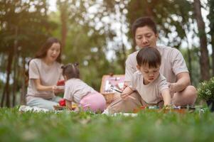 A caring Asian dad teaches his little son to draw on a canvas while enjoying a picnic in the park. photo