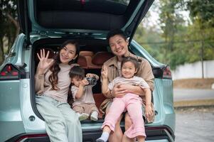 A happy and cheerful Asian family sitting in the trunk of their car, smiling at the camera. photo