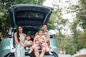 A happy Asian family sitting in the trunk of their car, enjoying their adventure together. photo
