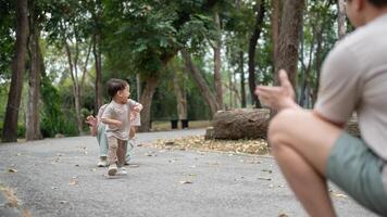 A cheerful, innocent little Asian boy runs happily to his dad, enjoying a game of tag in a park. photo