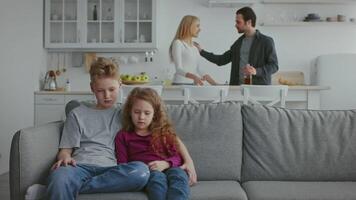 Tensions rise in a domestic setting as a couple argues about an issue, while two children sit quietly on the couch, observing the situation unfold in their home. video