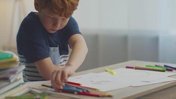 A preteen boy with ginger hair is focused on his studies at a desk, using a red marker to draw. He is surrounded by colorful stationery and textbooks, engaged in remote learning. video