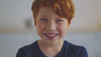 A preteen boy with ginger hair smiles while focusing on his studies. He participates in an online lesson, surrounded by a bright, inviting learning space, embodying the essence of remote education. video