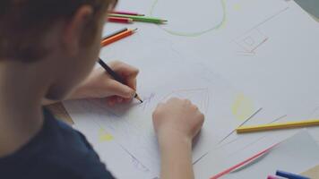 A preteen boy with ginger hair is deeply focused on his art assignment, using colored pencils to illustrate a scene while studying remotely from home. He is surrounded by various art supplies. video