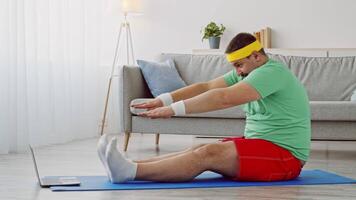 A man in comfortable workout attire practices stretches on an exercise mat in his living room. He focuses on his fitness while following an online workout program for weight loss. video