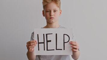 A young boy stands with a serious expression, holding a sign that reads HELP. This startling image reflects the urgent plea for assistance in a context of domestic violence. video