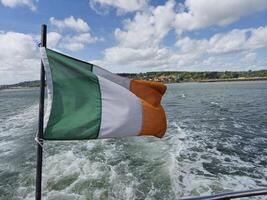 Irish Flag Fluttering Above a Scenic River Backdrop photo