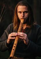 Long-haired Viking playing wooden flute carved with Nordic symbols in outdoor setting photo