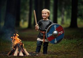Smiling young boy in Viking costume holding sword and shield near campfire in forest photo