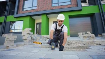 Builder laying a paving brick placing it on the sand foundation. Construction worker uses a level tool to precisely align paving stones during installation video