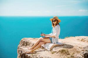 Freelance woman working on a laptop by the sea, typing away on the keyboard while enjoying the beautiful view, highlighting the idea of remote work. photo