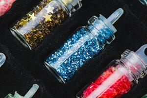 Glass Bottles with Different Types of Glitter, Gold Star-Shaped Glitter, Blue Glitter, and Red Shredded Glitter in a Black Foam Holder. Ideal for Crafting and Decorative Projects photo
