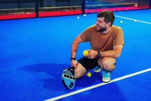 Man practices skills on vibrant blue court while holding paddle and balls during recreational session photo