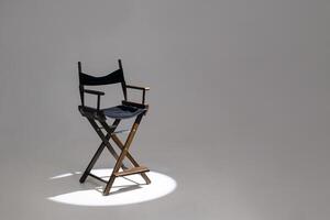 Directors chair stands in the beam of light. Space for text. Vacant chair. The concept of selection and casting. Shadow and light. photo