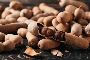Pile of fresh tamarind fruits in shell close up on wood background photo