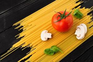 Spaghetti with tomato, mushrooms and spinach on black background. Top view. Healthy eating concept. Preparation of products photo