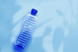 Clear plastic water bottle with blue cap on light blue background with soft leaf shadow, copyspace. Minimal top view, themes of ecology, recycling, sustainable living, reduce disposable plastics photo