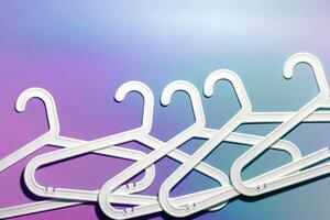 Top view minimal style pattern of white plastic hangers with hook on purple blue background. Flatlay with Clothes racks for hanging garments. Minimal trend photo, lifestyle or interior design content photo