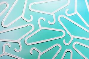 White Plastic hangers as minimal pattern on teal gradient background, Clothes rack for organizing clothes in closets or retail stores for hanging of garments, top view, fashion, organization content photo