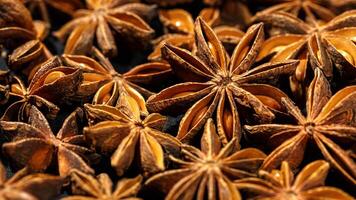 Brown Anise stars as pattern at sunlight, close up aromatic spices dried aniseed on black background, aesthetic food pattern, textural graphic banner, natural season condiments photo