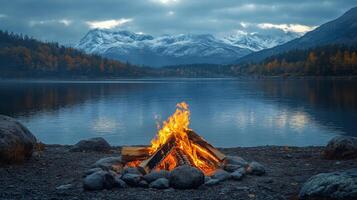 A campfire is lit in front of a lake and mountains photo