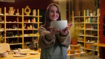 femelle potier artiste sculpteur travail avec argile Maître classe céramique atelier caucasien souriant femme fille création pot Fait main assiette montrant à caméra petit affaires propriétaire artisanat boutique fabrication video